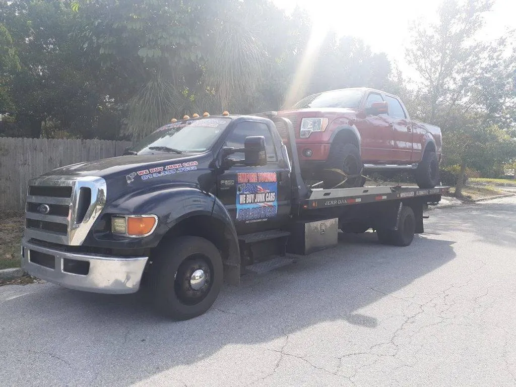 Empire Towing black Ford F-650 flatbed carrying a red pickup on a sunny residential street