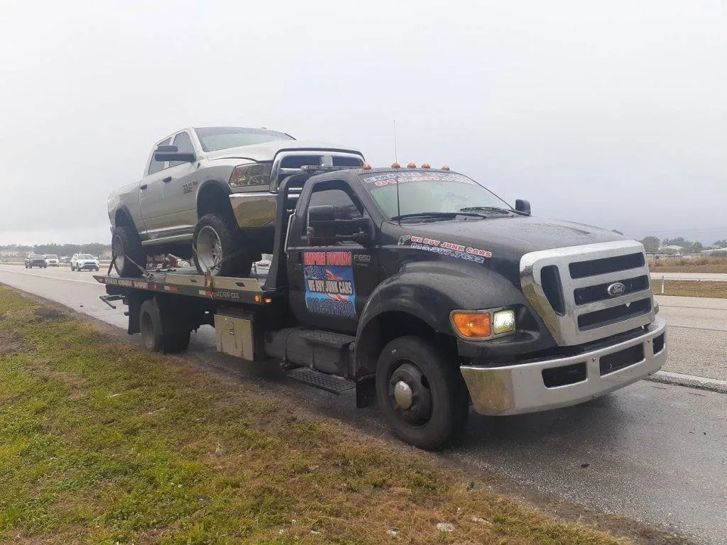 Empire Towing flatbed loaded with a silver pickup on a wet highway shoulder