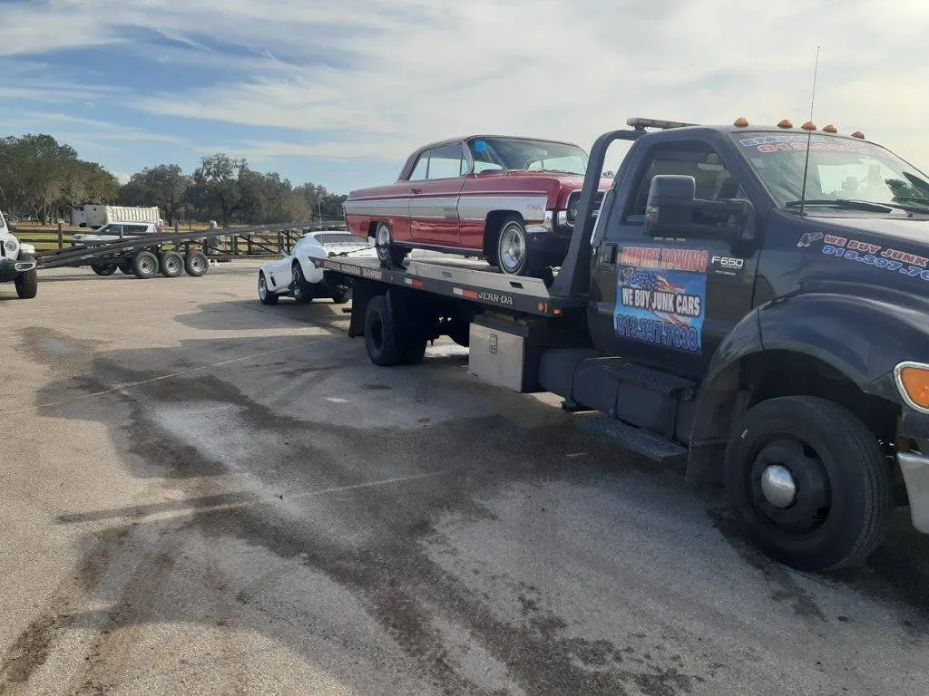 A red classic car sits on the Empire Towing flatbed in a storage yard