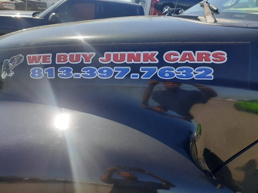 We Buy Junk Cars decal on the black truck body, shot in bright sunlight