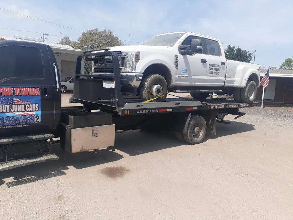 Empire Towing flatbed hauling a white Ford F-350 dually pickup in a sunlit lot